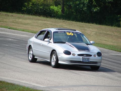 1993 Ford Taurus - This silver sedan, possibly a 1999 model, navigates a turn on a road course with racing stripes and a prominent number 50 displayed.