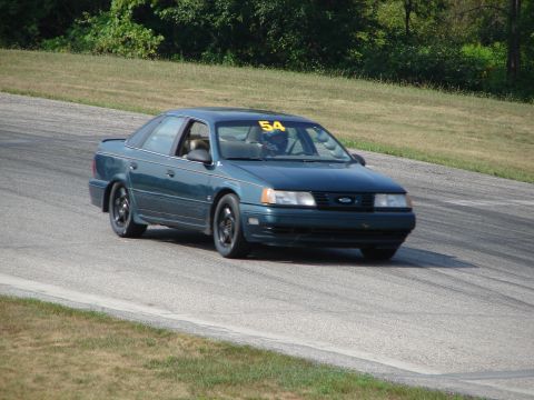 1993 Ford Taurus - A dark green 1993 Ford Taurus competes on a road course, displaying the number 54 on its windshield.