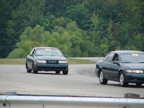 1993 Ford Taurus - Two sedans compete on a road course, with racing numbers visible on their windshields.