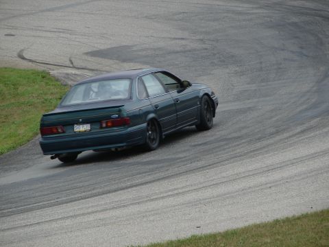 1993 Ford Taurus - A dark green 1993 Ford Taurus SHO Plus drifts around a corner on a race track.