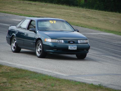 1993 Ford Taurus - A dark green sedan with racing number 57 on the windshield navigates a turn on a paved track.