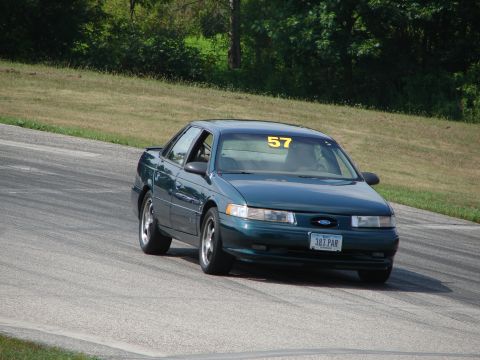 1993 Ford Taurus - A dark green sedan, possibly a 1992 model, navigates a turn on a road course with racing number 57 displayed.