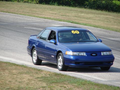 1993 Ford Taurus - A blue 1993 Ford Taurus sedan navigates a turn on a road course, displaying the number 60 on its windshield.