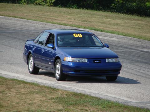 1993 Ford Taurus - A blue 1993 Ford Taurus navigates a turn on a road course, displaying the number 60 on its windshield.