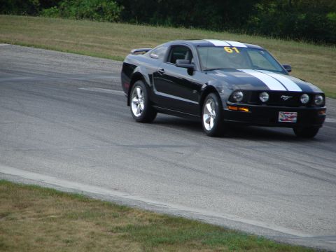 1993 Ford Taurus - A black Ford Mustang with white racing stripes navigates a turn on a paved race track.