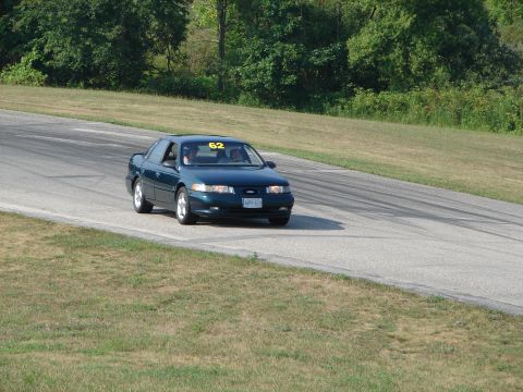 1993 Ford Taurus - A dark green sedan, possibly a 1995 model, navigates a turn on a race track with the number 62 displayed.