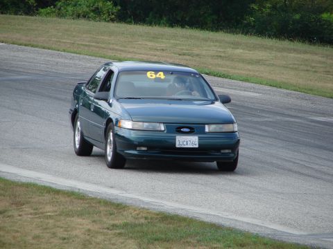 1993 Ford Taurus - Green 1993 Ford Taurus driving on a road course with racing number 64 displayed.