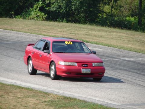 1993 Ford Taurus - A red 1993 Ford Taurus competes on a road course, displaying the number 69 on its windshield.