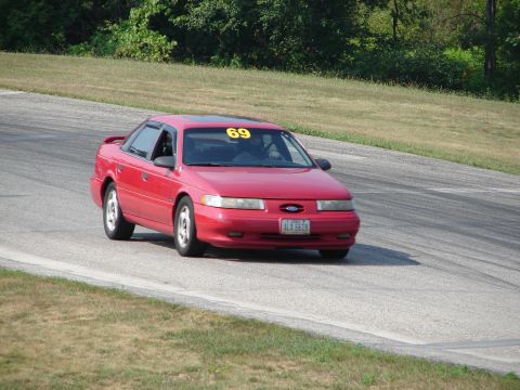 1993 Ford Taurus - A red 1993 Ford Taurus is captured on the track, displaying the number 69 on its windshield.