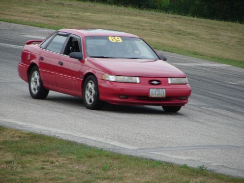 1993 Ford Taurus - A red sedan with a racing number on its windshield navigates a turn on a road course.