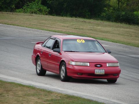 1993 Ford Taurus - A red 1993 Ford Taurus with racing number 69 on the windshield navigates a turn on a road course.