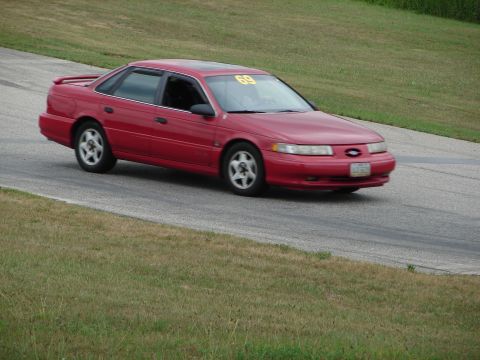 1993 Ford Taurus - A red 1993 Ford Taurus is seen on a race track with a racing number displayed on its windshield.