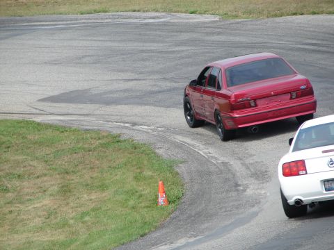 1993 Ford Taurus - Red 1993 Ford Taurus navigates a turn on a road course, with another vehicle in view.