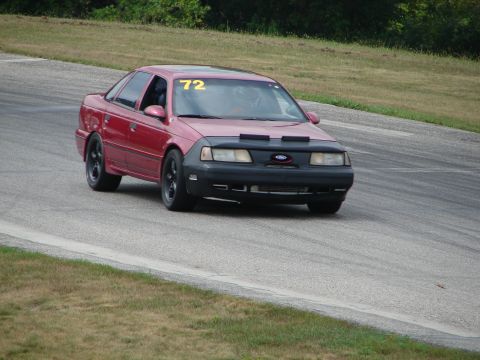1993 Ford Taurus - A red sedan with a racing number on its windshield navigates a turn on a paved track.