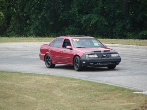 1993 Ford Taurus - A red 1993 Ford Taurus is seen on a road course, displaying the number 72 on its windshield.