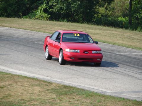 1993 Ford Taurus - A red 1993 Ford Taurus competes on a road course, displaying the number 73 on its windshield.