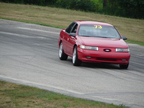 1993 Ford Taurus - A red sedan, likely a 1992 Ford Taurus, navigates a turn on a road course, displaying the number 73.