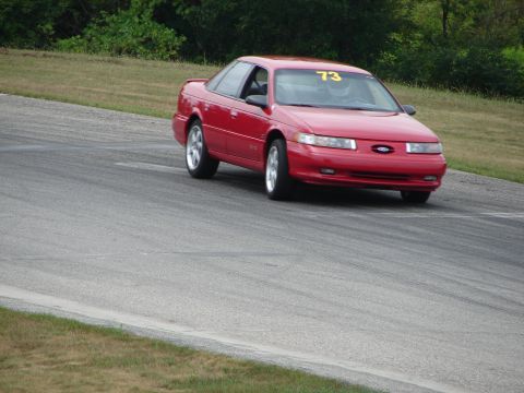 1993 Ford Taurus - A red 1993 Ford Taurus, marked with racing number 73, navigates a turn on a road course.