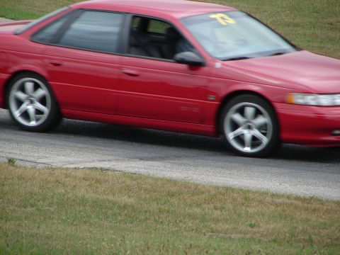 1993 Ford Taurus - Red 1993 Ford Taurus sedan with racing number 73 on windshield, captured mid-corner on a track.