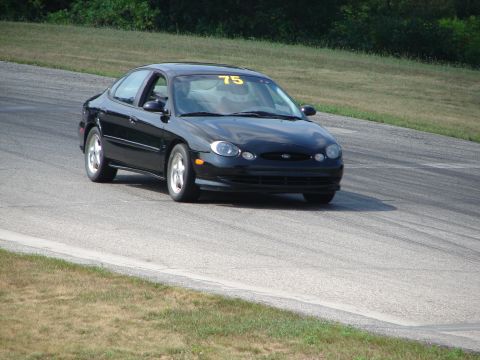 1993 Ford Taurus - A black sedan with a racing number on its windshield navigates a turn on a paved track.