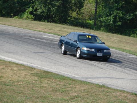 1993 Ford Taurus - A teal 1993 Ford Taurus navigates a turn on a road course, displaying the number 78 on its windshield.