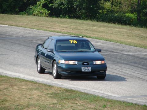 1993 Ford Taurus - A dark green sedan, likely a 1996 Ford Taurus, navigates a turn on a road course with the number 78 displayed.