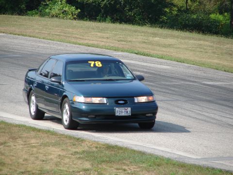 1993 Ford Taurus - A dark blue 1993 Ford Taurus with racing number 78 on the windshield navigates a turn on a road course.