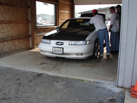 1993 Ford Taurus - A white sedan with a black hood is parked in a garage, with people attending to it.