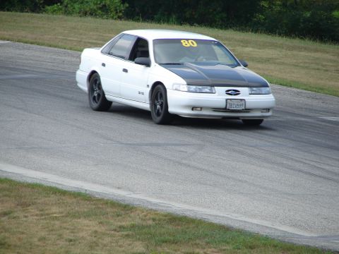 1993 Ford Taurus - A white sedan with a black hood and racing number 80 navigates a turn on a paved track.
