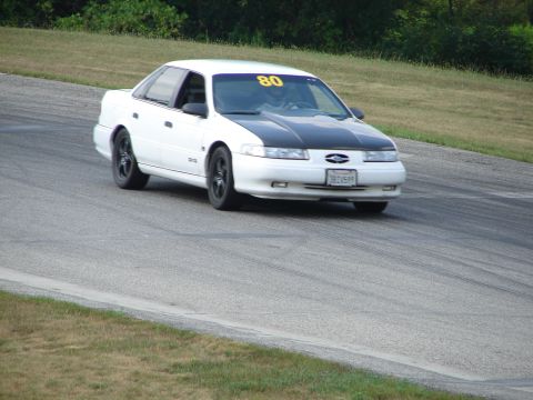 1993 Ford Taurus - White 1993 Ford Taurus with a black hood and racing number 80 navigates a turn on a road course.