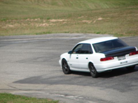 1993 Ford Taurus - A white 1993 Ford Taurus sedan with a black trunk lid navigates a turn on a road course.