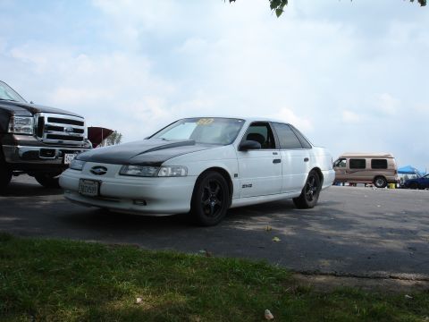 1993 Ford Taurus - White 1993 Ford Taurus with aftermarket black hood and wheels, parked outdoors.