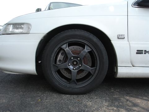1993 Ford Taurus - Close-up of a white car's front wheel, showing custom rims and brake calipers.