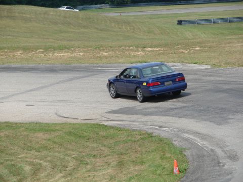 1993 Ford Taurus - A blue sedan navigates a turn on a road course, with another white vehicle visible in the background on a grassy incline.