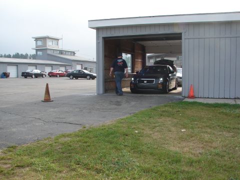 1993 Ford Taurus - A person walks away from a black Cadillac as it exits a garage at what appears to be a race track.