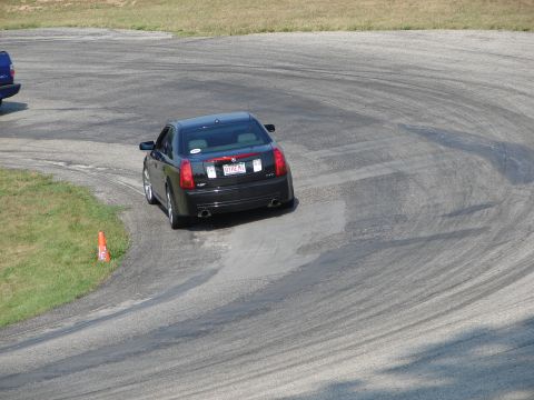 1993 Ford Taurus - Black Cadillac sedan drifts around a corner on a paved race track, with another vehicle visible.