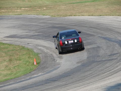 1993 Ford Taurus - A black Cadillac sedan navigates a turn on a race track, leaving tire marks on the asphalt.