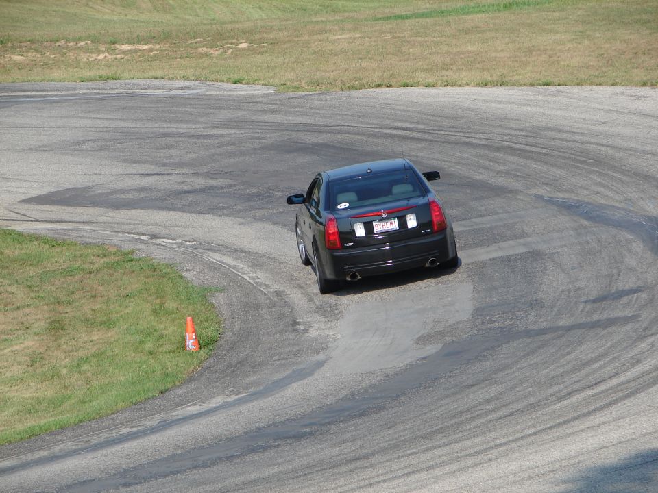 Black Cadillac sedan drifting on a race track, tire marks visible on the asphalt