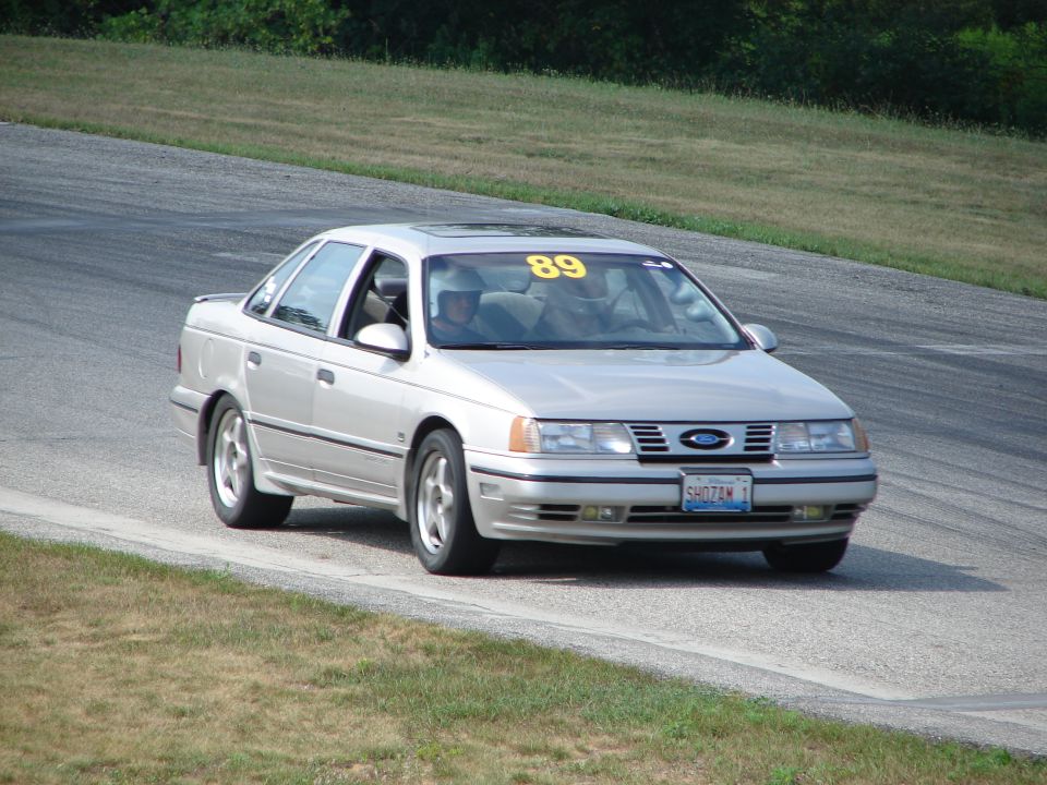 Silver 1993 Ford Taurus with number 89 on windshield driving on a race track
