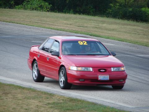 1993 Ford Taurus - A red sedan with a racing number on its windshield navigates a turn on a paved track.