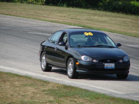 1993 Ford Taurus - A black sedan with a racing number on its windshield navigates a turn on a paved track.