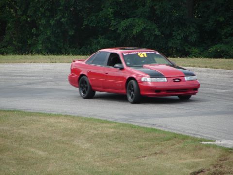 1993 Ford Taurus - A red 1993 Ford Taurus with a black hood stripe navigates a turn on a road course, displaying racing number 97.