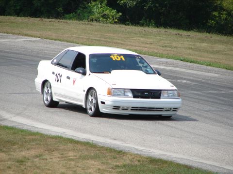 1993 Ford Taurus - A white 1993 Ford Taurus with racing numbers navigates a turn on a road course.