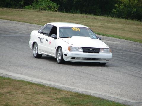 1993 Ford Taurus - A white 1993 Ford Taurus with racing numbers navigates a turn on a paved track.