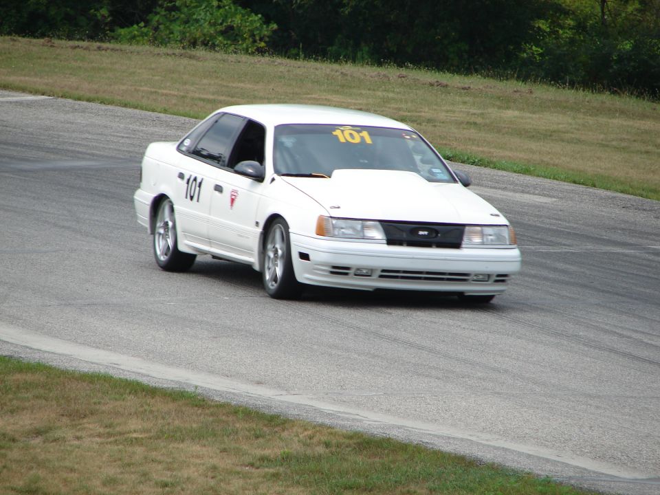 White 1993 Ford Taurus with number 101 on door and windshield driving on a race track