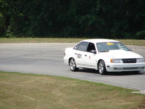 1993 Ford Taurus - A white sedan, likely a 1992 model, navigates a turn on a race track, displaying racing numbers.