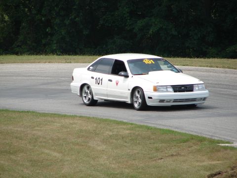 1993 Ford Taurus - A white 1993 Ford Taurus, marked with racing number 101, navigates a turn on a road course.