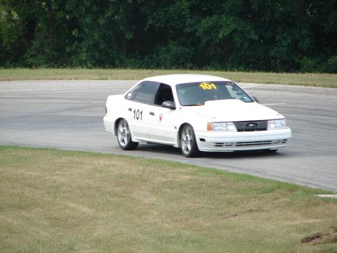 1993 Ford Taurus - White 1993 Ford Taurus with racing numbers on a track during a sunny day.