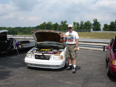 1993 Ford Taurus - A man poses with a white car that has its hood open, revealing the engine bay, at what appears to be a race track.