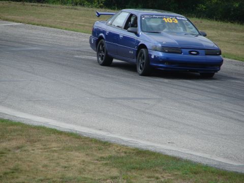 1993 Ford Taurus - A blue 1993 Ford Taurus SHO races on a track, displaying the number 103 on its windshield.